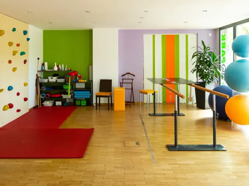 Bewegungsraum der Praxis Tempelhof mit Kletterwand, Gehbarren und Therapiebällen